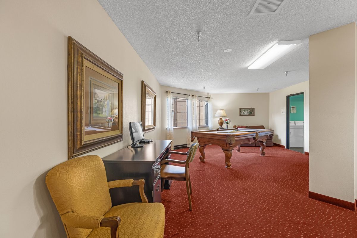 A spacious room featuring a pool table, desk, chairs, and wall art.