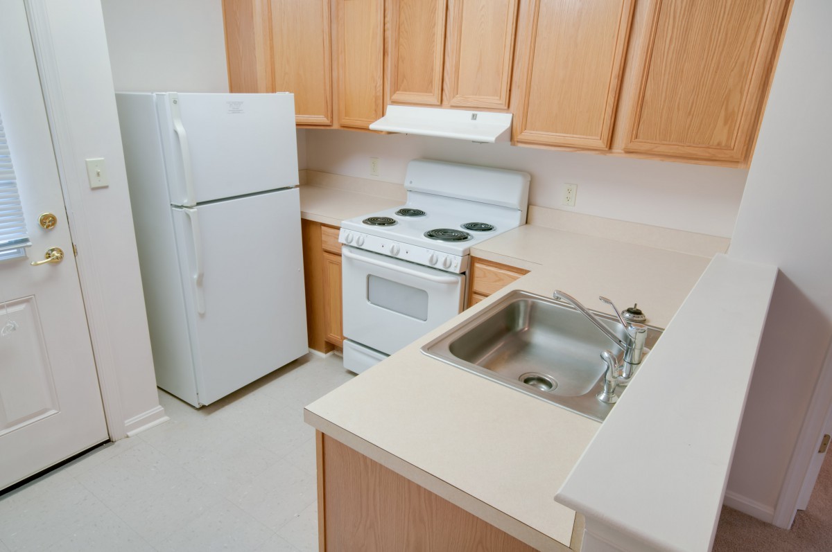 A compact kitchen with wooden cabinets, a fridge, stove, and sink.