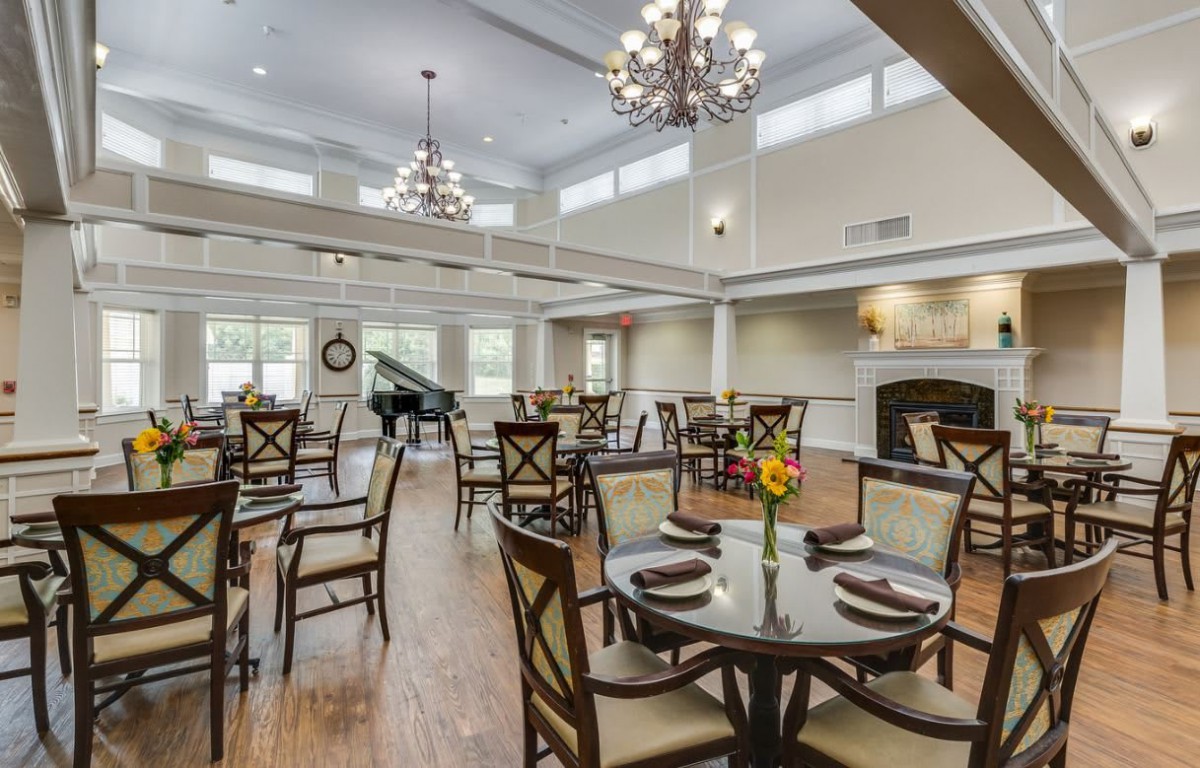 An elegant dining room with chandeliers, a grand piano, and neatly arranged tables and chairs.