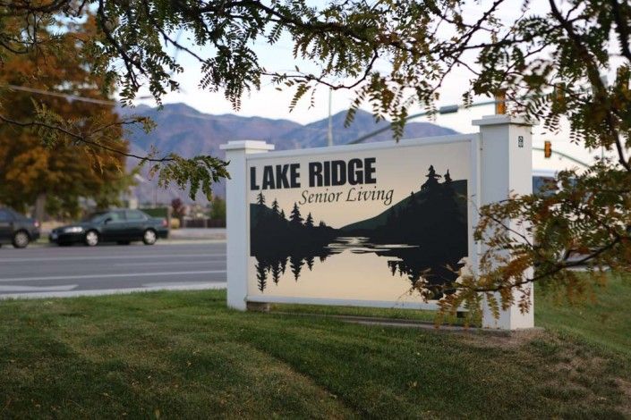 A sign for Lake Ridge Senior Living with a scenic nature design in the foreground.