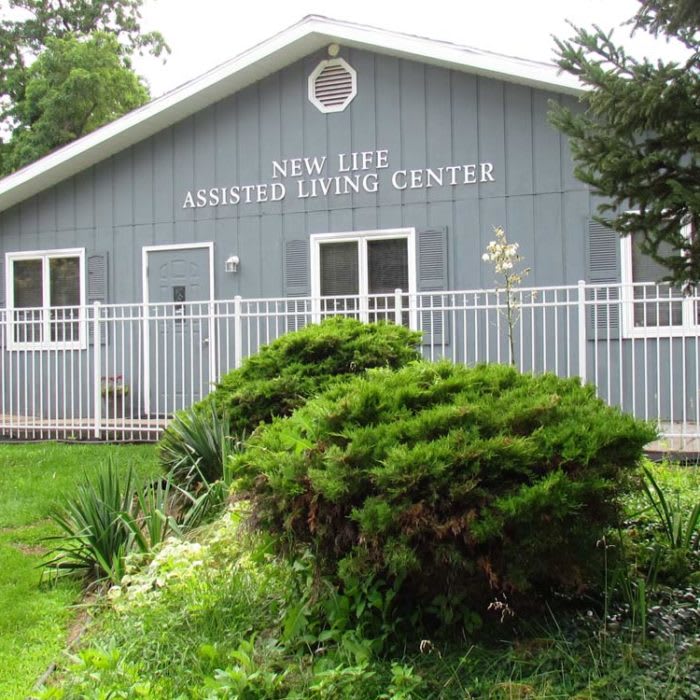A building labeled 'New Age Family Living Center' surrounded by bushes and a white fence.