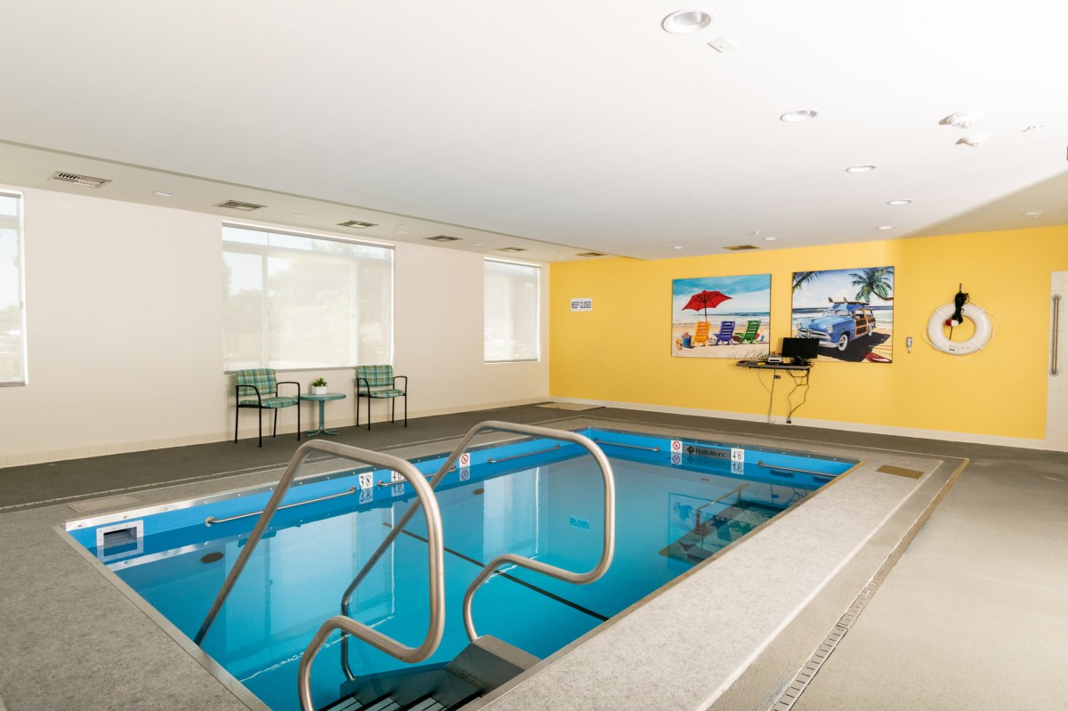 An indoor swimming pool with surrounding chairs and bright yellow walls adorned with artwork.