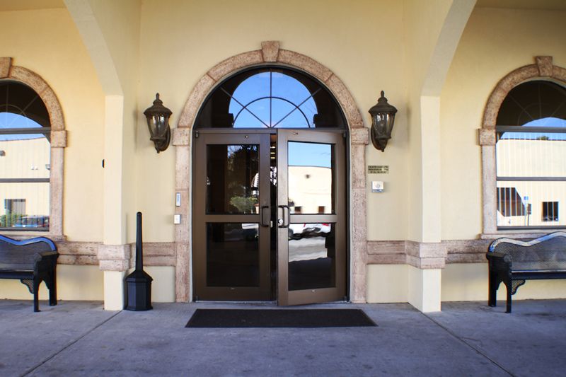 A building entrance featuring double glass doors and an arched design, flanked by decorative lights.