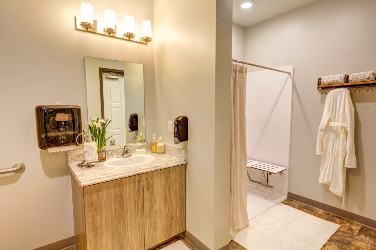 A modern bathroom featuring a wooden vanity with a sink and mirror, accompanied by a light fixture above. The shower area is enclosed with a curtain.