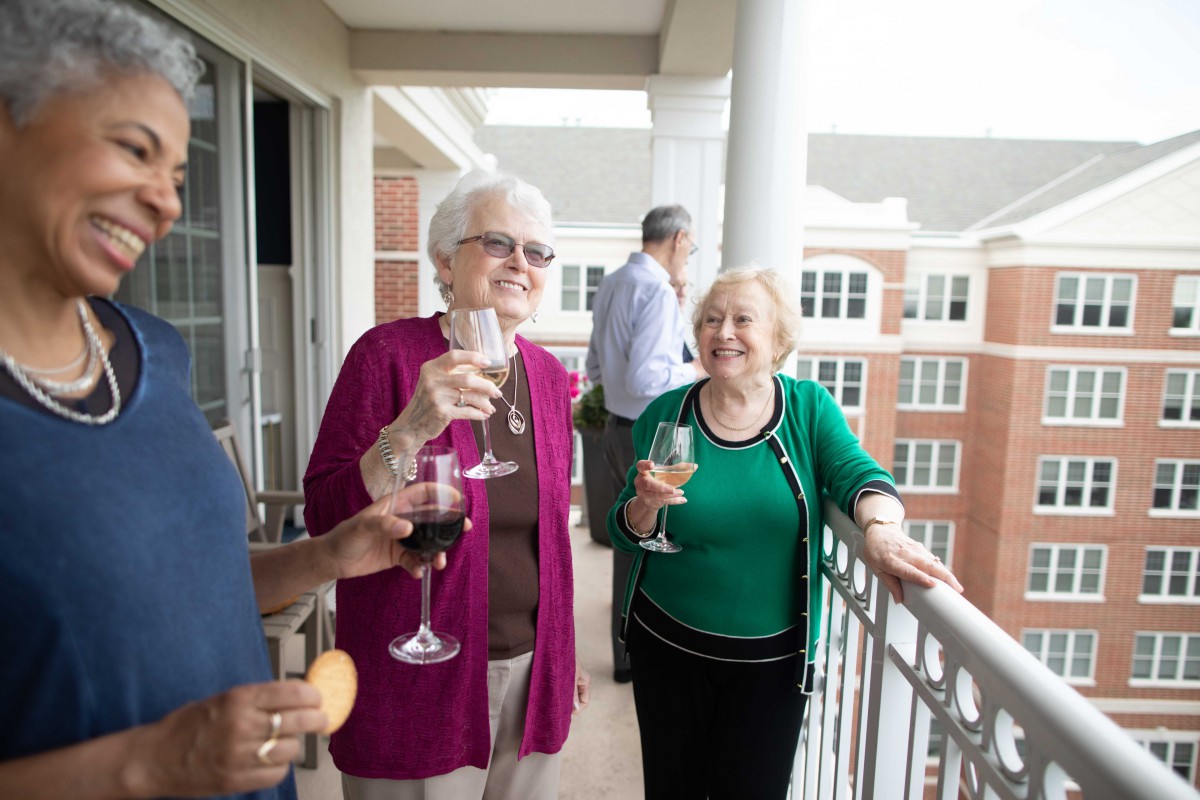 A group of seniors enjoying drinks and socializing on a balcony during the daytime.