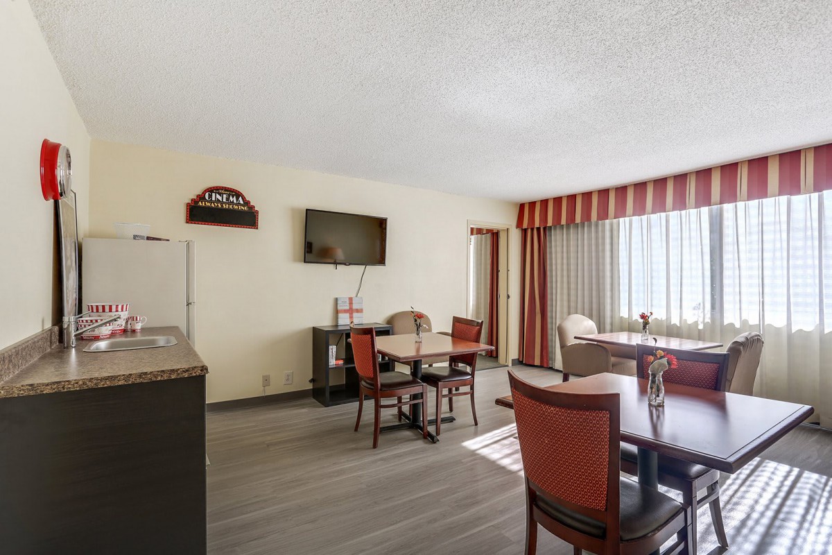 A bright hotel dining area with tables, chairs, and a wall-mounted TV.