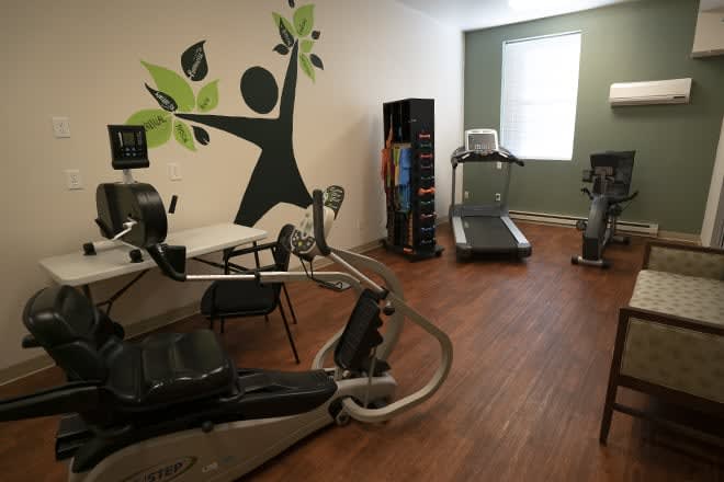 A small fitness room featuring a treadmill, stationary bike, and exercise machine.