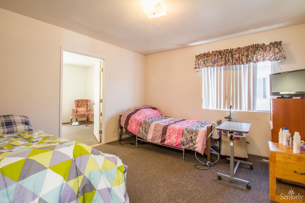 A simple care facility room with two beds and a window, providing a cozy environment.