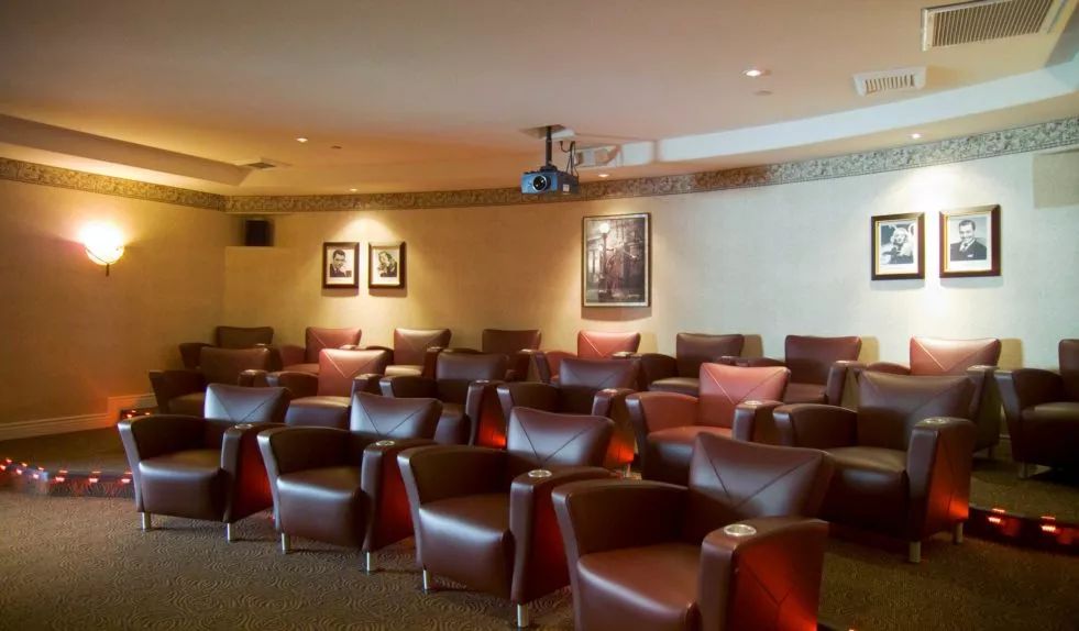 A cozy theater room with rows of leather chairs and a ceiling-mounted projector.