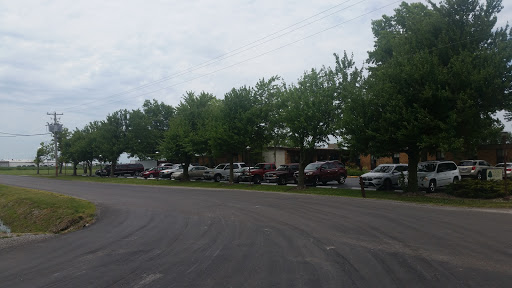 A view of a street lined with parked vehicles and lush green trees under a cloudy sky.
