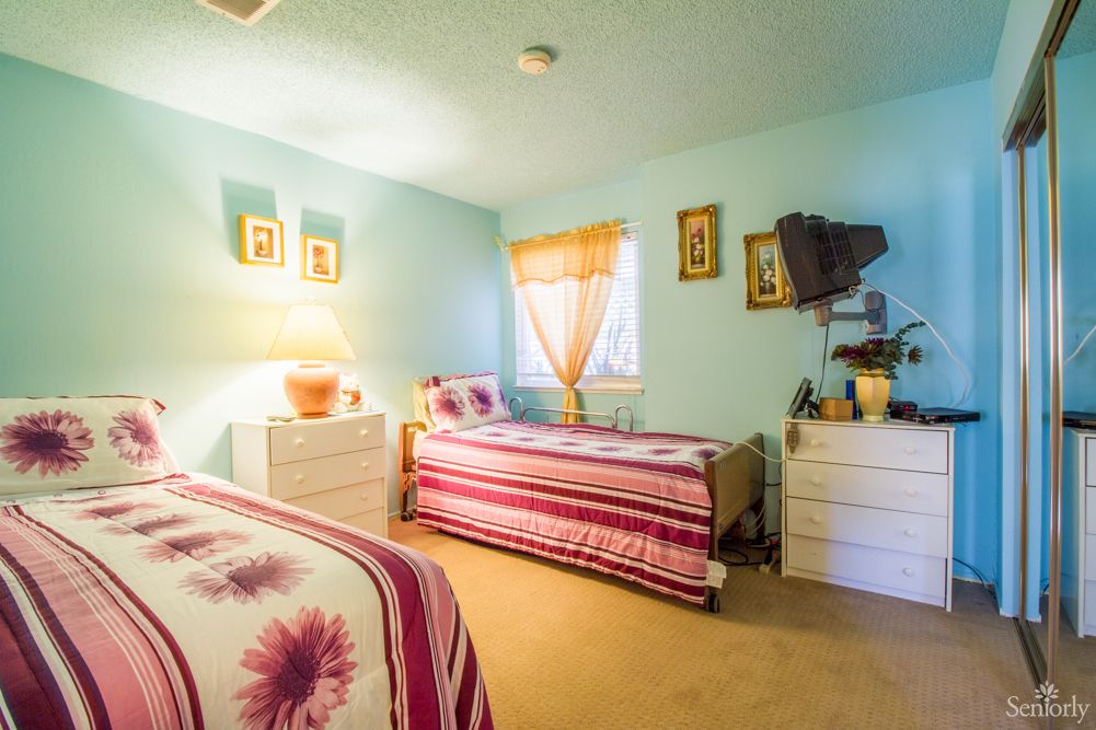 A cozy bedroom with twin beds, decorated in soft colors, featuring natural light from a window with drapes.