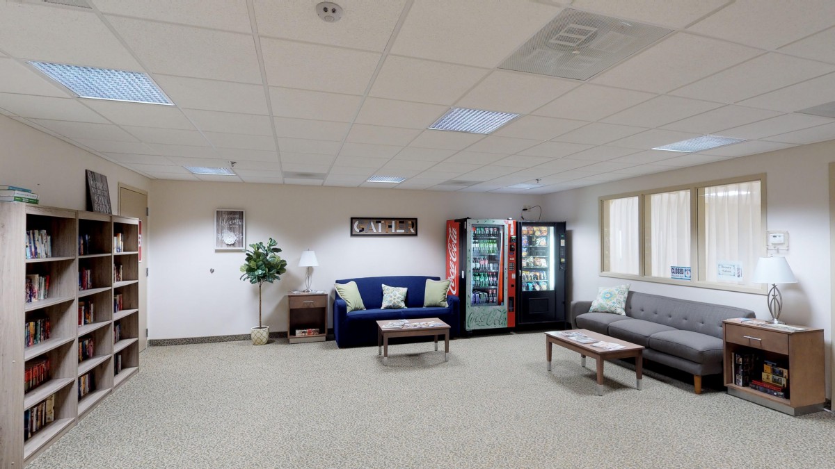 A spacious waiting room with sofas, vending machines, and an indoor plant.