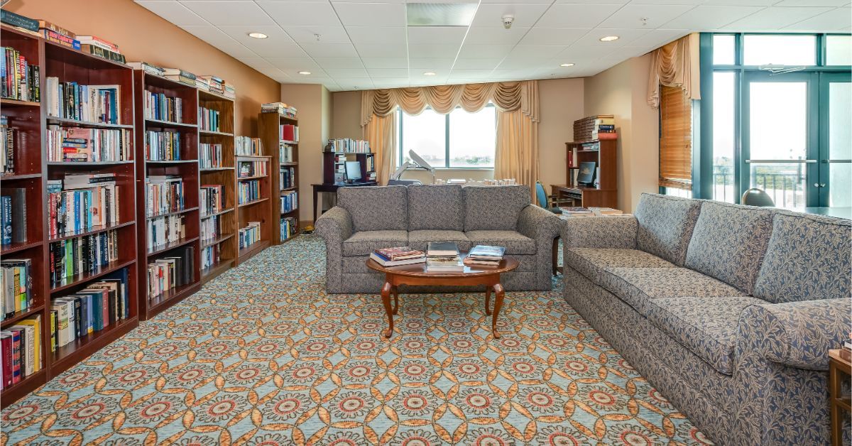 A cozy living room with bookshelves, comfortable seating, and a patterned carpet.