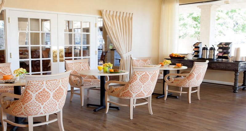 A cozy dining area with stylish chairs and tables, decorated with flowers and bathed in natural light.