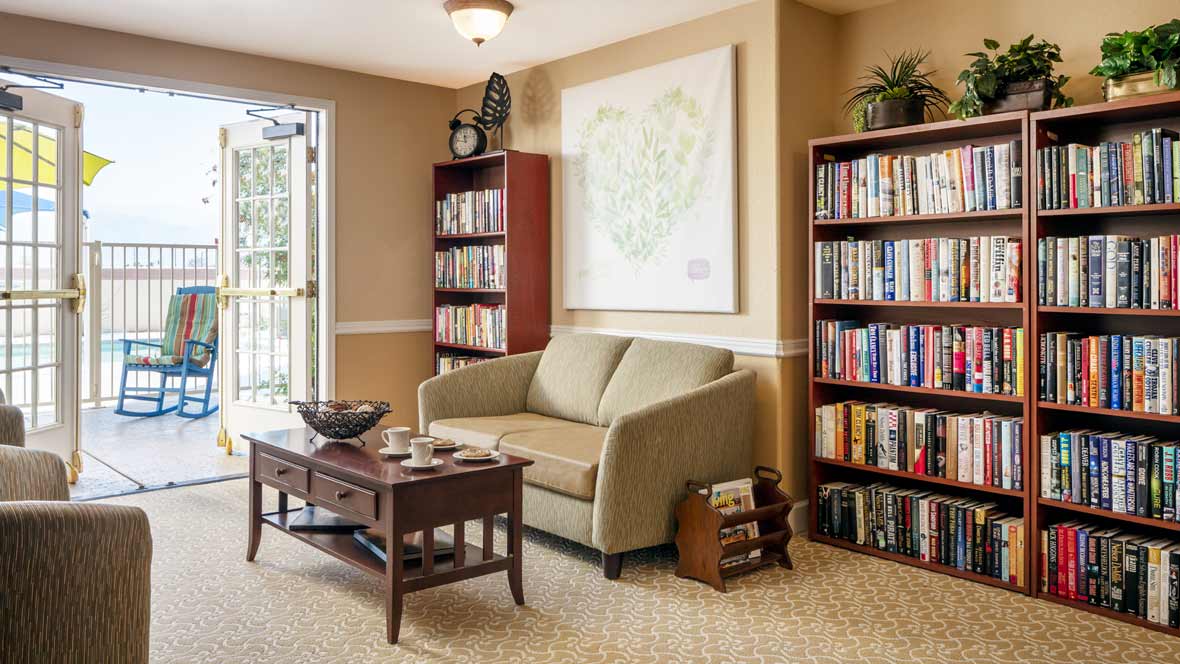 A cozy living room with a comfortable sofa, surrounded by bookshelves filled with books and a wooden coffee table in the center.