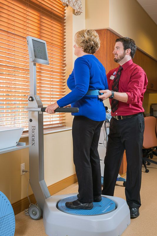 A healthcare professional assists a patient using a balance training machine in a rehabilitation session.
