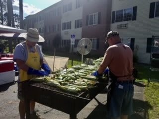 People grilling corn outdoors at a summer event.