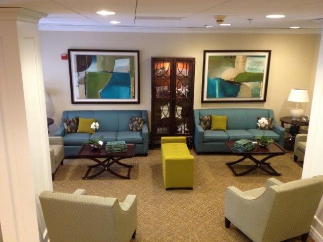 A modern lobby with blue sofas, white armchairs, and abstract wall art creates a welcoming waiting area.