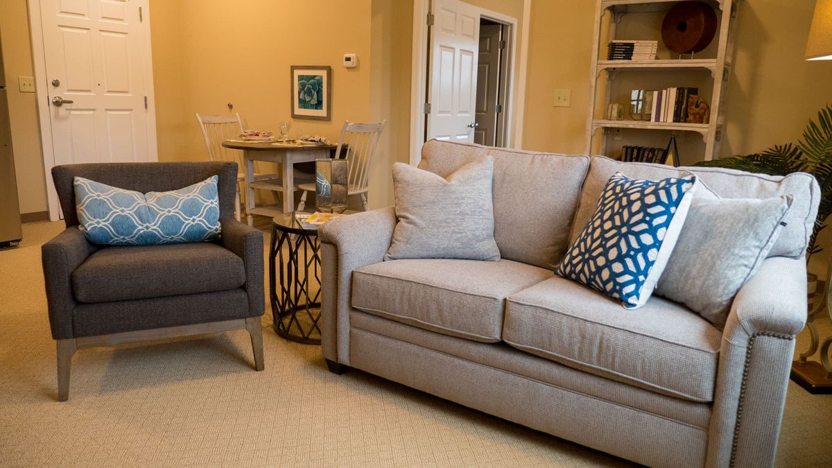 A cozy living room with a beige sofa, armchair, and decorative pillows, featuring a modern coffee table and stylish decor.