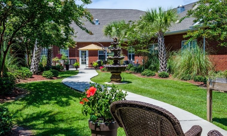 A beautifully landscaped garden with a fountain and pathway leading to a brick building.