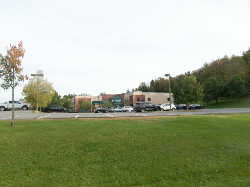 A view of a commercial building with a parking lot surrounded by grass and trees under a cloudy sky.