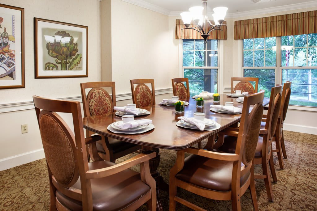 An elegant dining room with a set table and wooden chairs, featuring a window view.