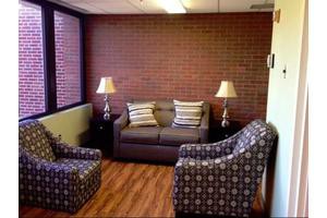 A cozy living room with a sofa, two patterned armchairs, and two lamps against a brick wall.