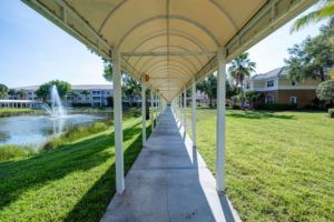 A symmetrical covered walkway in a sunny outdoor setting, with grass and a fountain nearby.