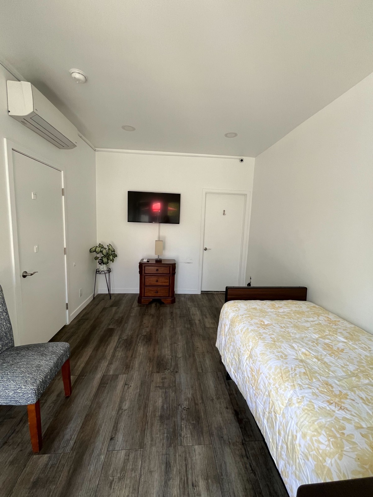 A minimalist bedroom with a single bed, hardwood floor, and a TV mounted on the wall.
