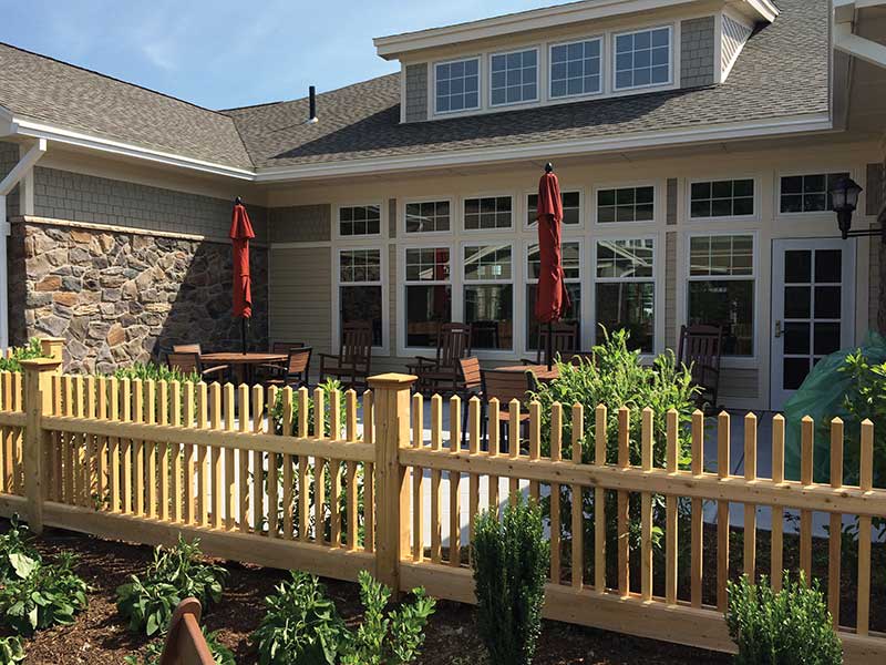 A cozy patio area with a wooden fence and garden, featuring large windows and red umbrellas.