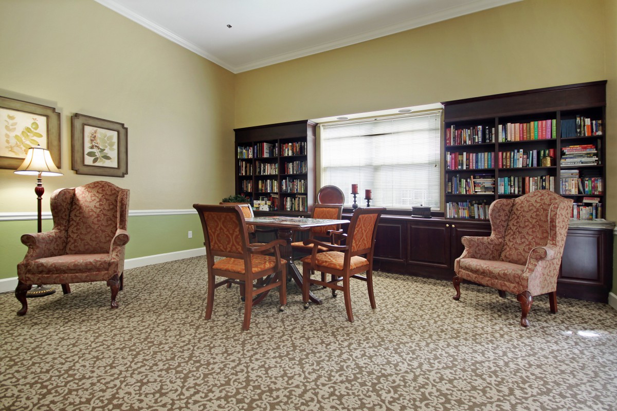 A cozy library room with a central table, surrounded by bookshelves and chairs.