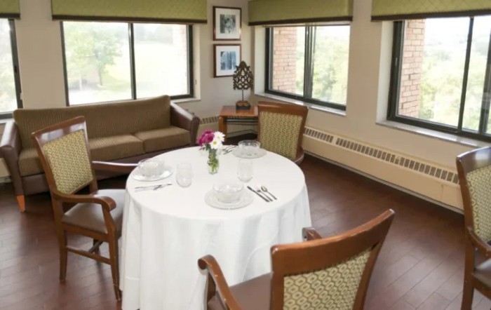 A cozy dining area with a round table set for two, featuring a sofa and large windows.