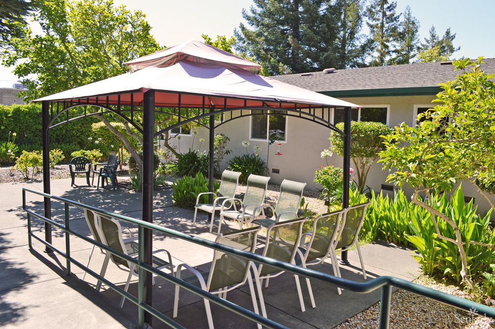 A cozy outdoor patio with a gazebo, chairs, and table surrounded by lush greenery.