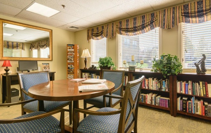 A well-lit meeting room with a wooden table, chairs, and a bookshelf near the windows.