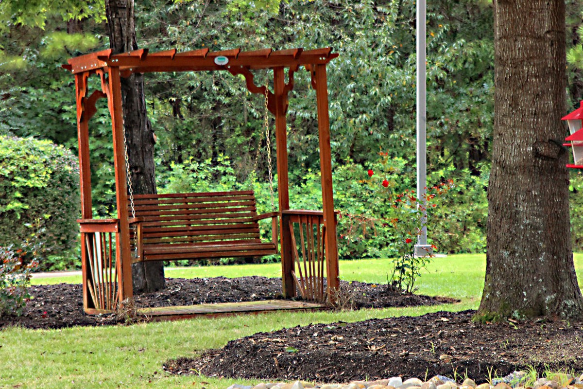 A wooden swing bench in a lush garden setting.