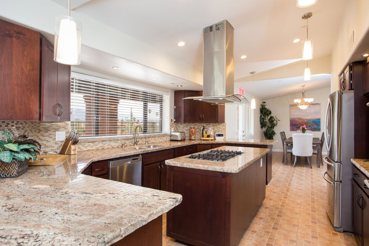A modern kitchen with granite countertops and a central island, featuring stainless steel appliances and rich wood cabinetry.