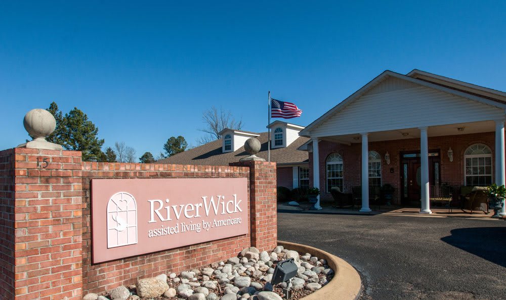 Entrance of RiverWick assisted living facility with a visible sign and flag.
