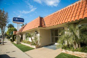 A sunny day view of a motel with a red tile roof and blue signage.