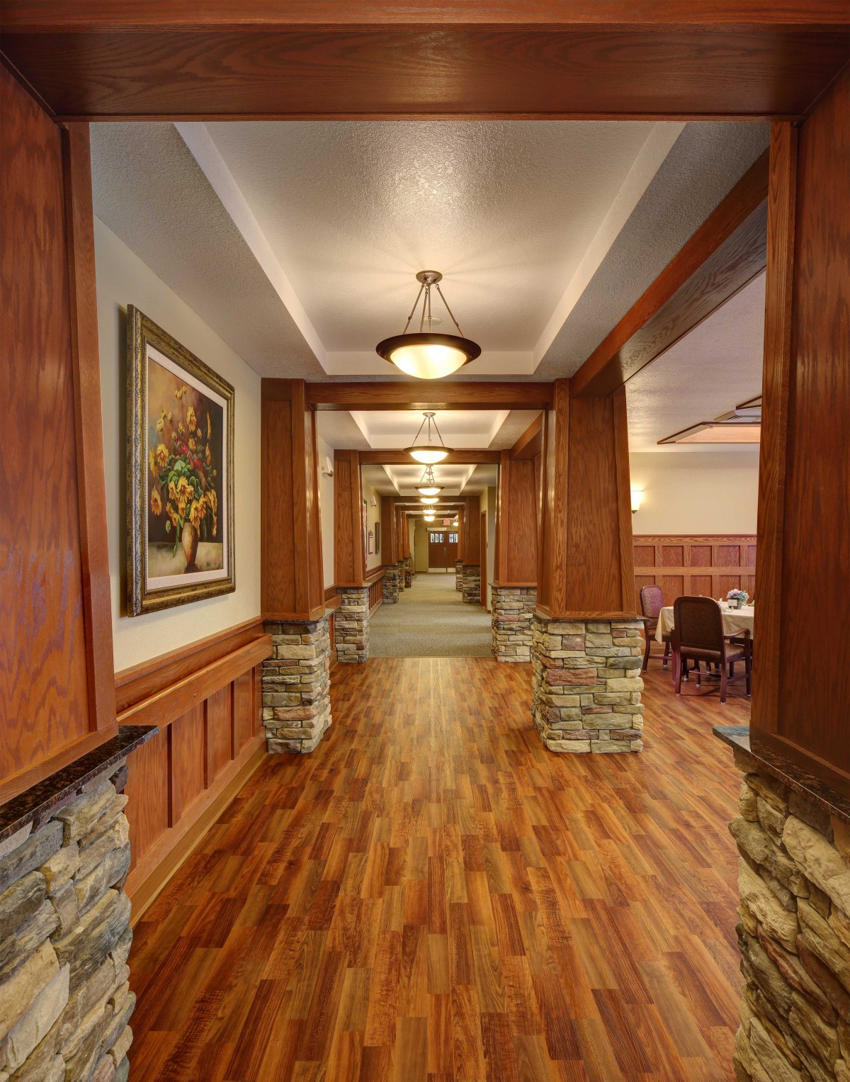 A warmly lit hallway with wooden flooring and stone-accented columns.