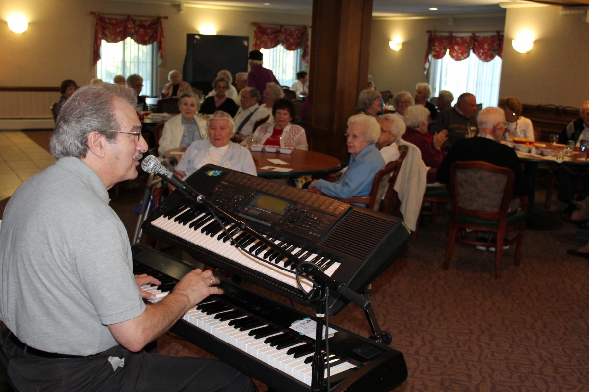 A musician performs on a keyboard for an attentive audience in an indoor setting.