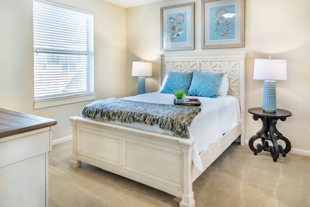 A cozy bedroom featuring a white bed with blue accent pillows, decorative artwork, and soft lighting.