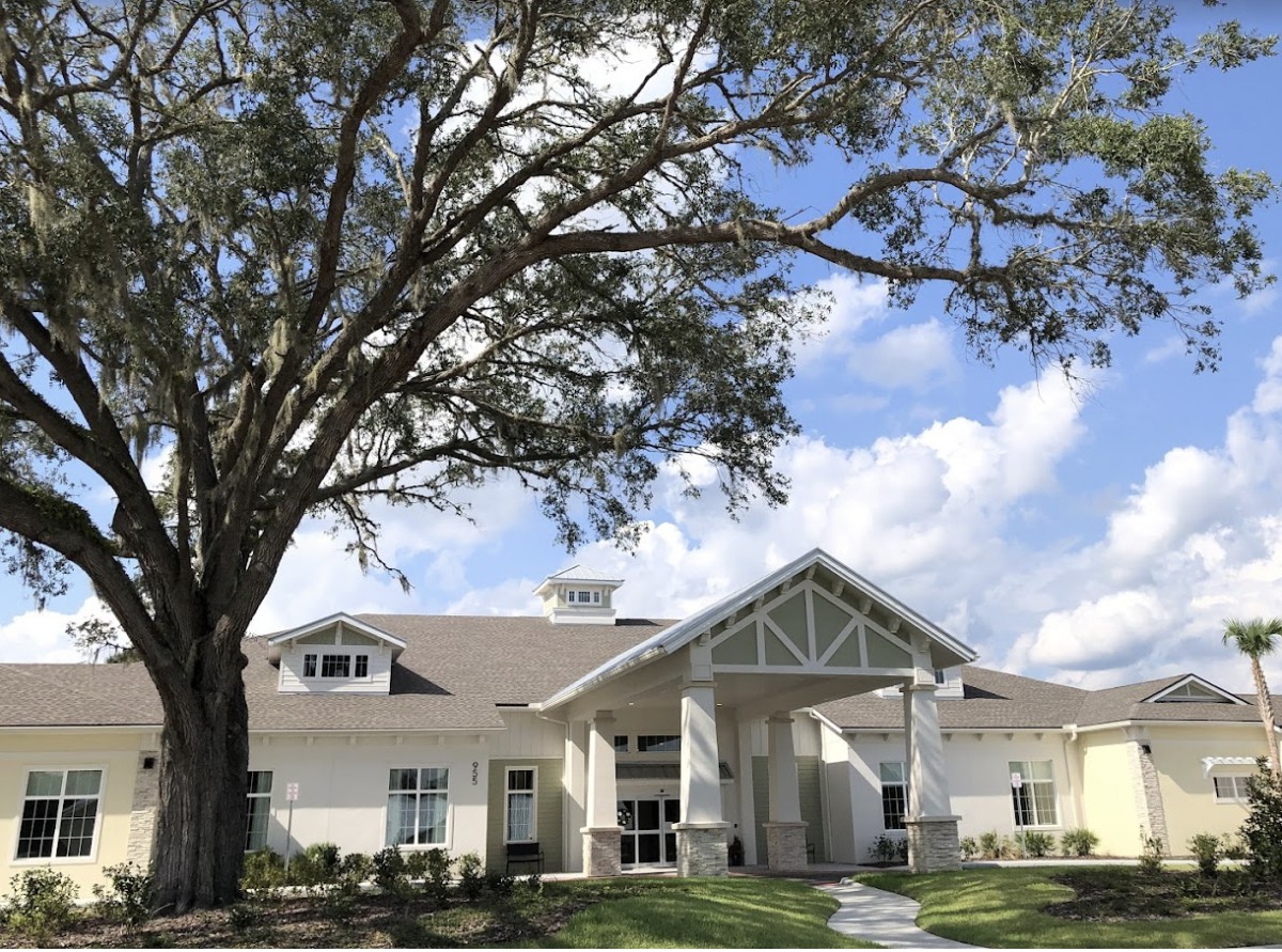 A modern building with a large tree in front, set against a partly cloudy sky.