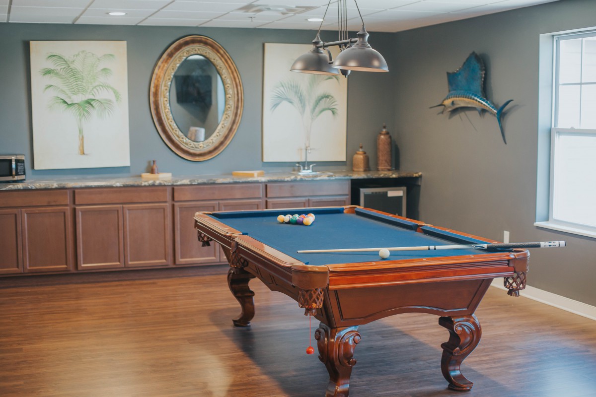 A stylish billiard room featuring a pool table with blue felt, hardwood floors, and elegant decor including a mirror and artwork.