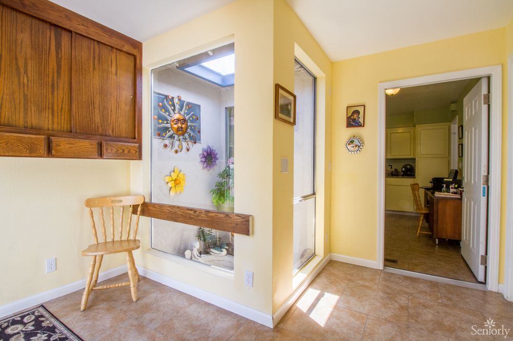 A bright interior with yellow walls, featuring a kitchen area connected to a sunlit room decorated with sun motifs and plants.