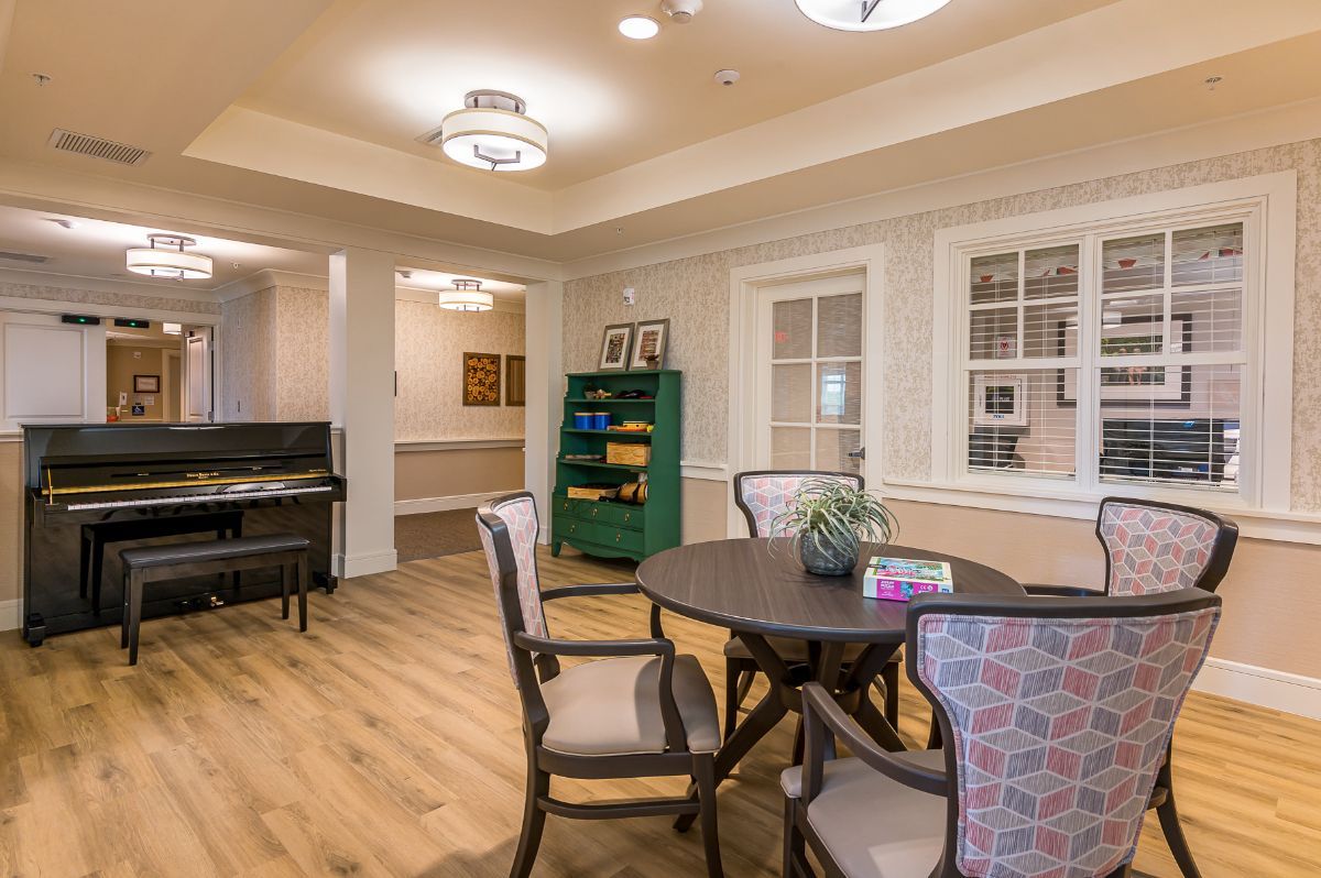 A cozy room with a round table, chairs, a bookshelf, and a piano.