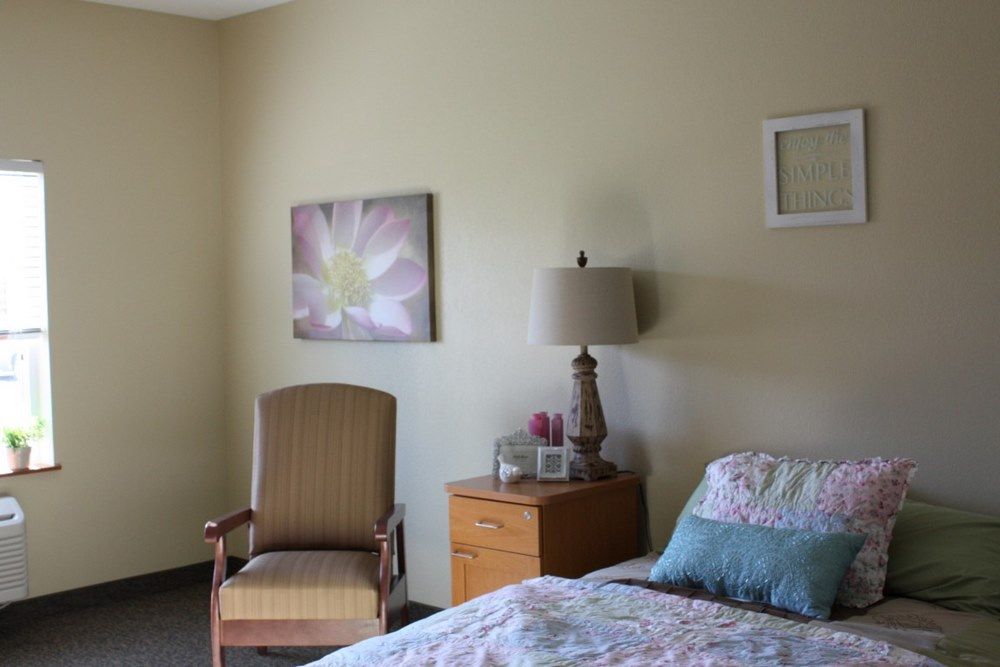 A cozy bedroom with a bed, wooden nightstand, lamp, and an upholstered chair.