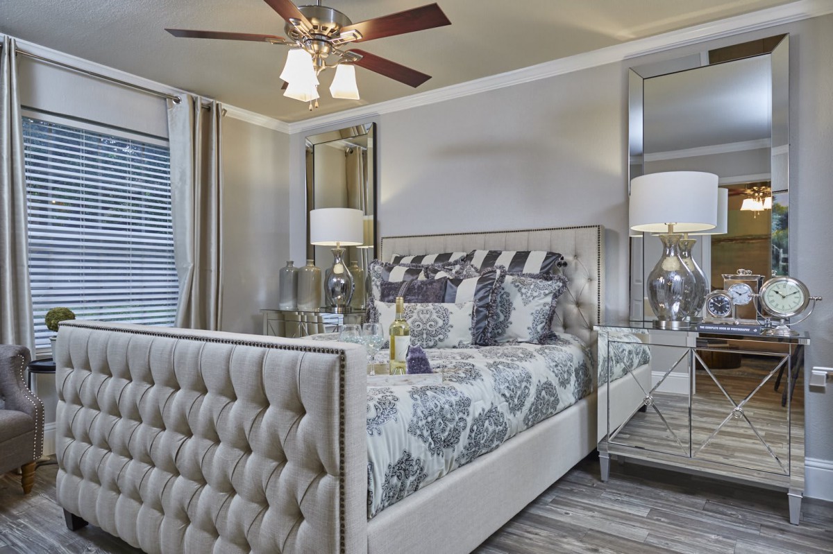 A modern, well-decorated bedroom featuring a tufted bed, elegant lamps, and a ceiling fan.