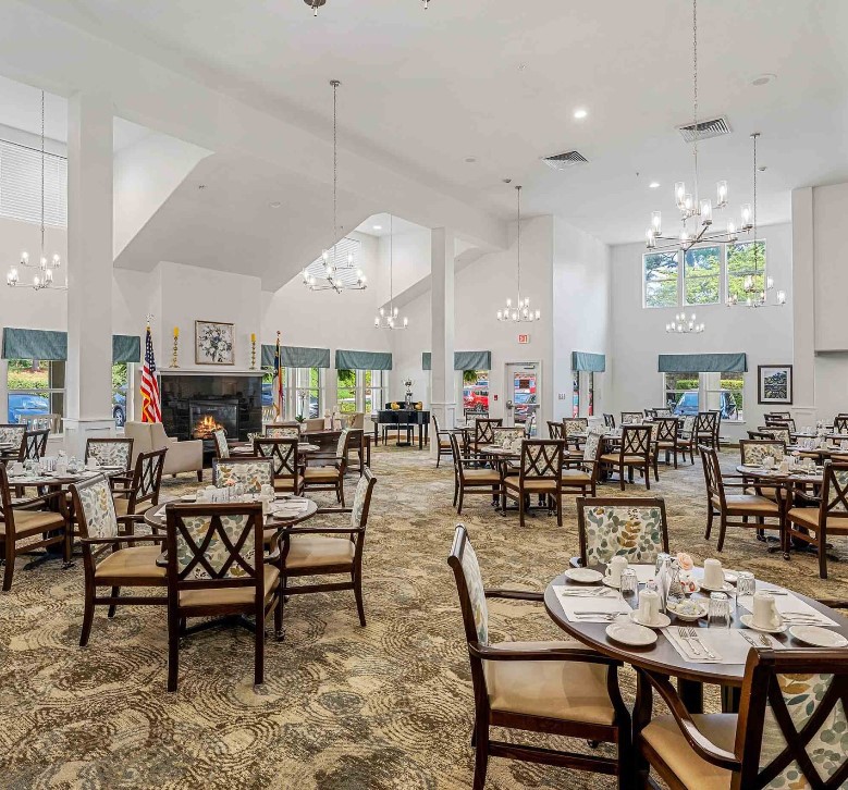 A spacious and elegantly decorated dining room featuring multiple tables and chairs, with chandeliers adding to the ambiance.