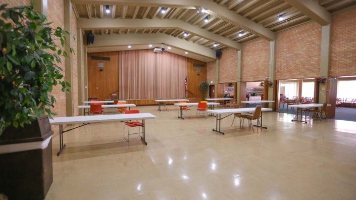 An empty hall with tables and chairs arranged in front of a stage.