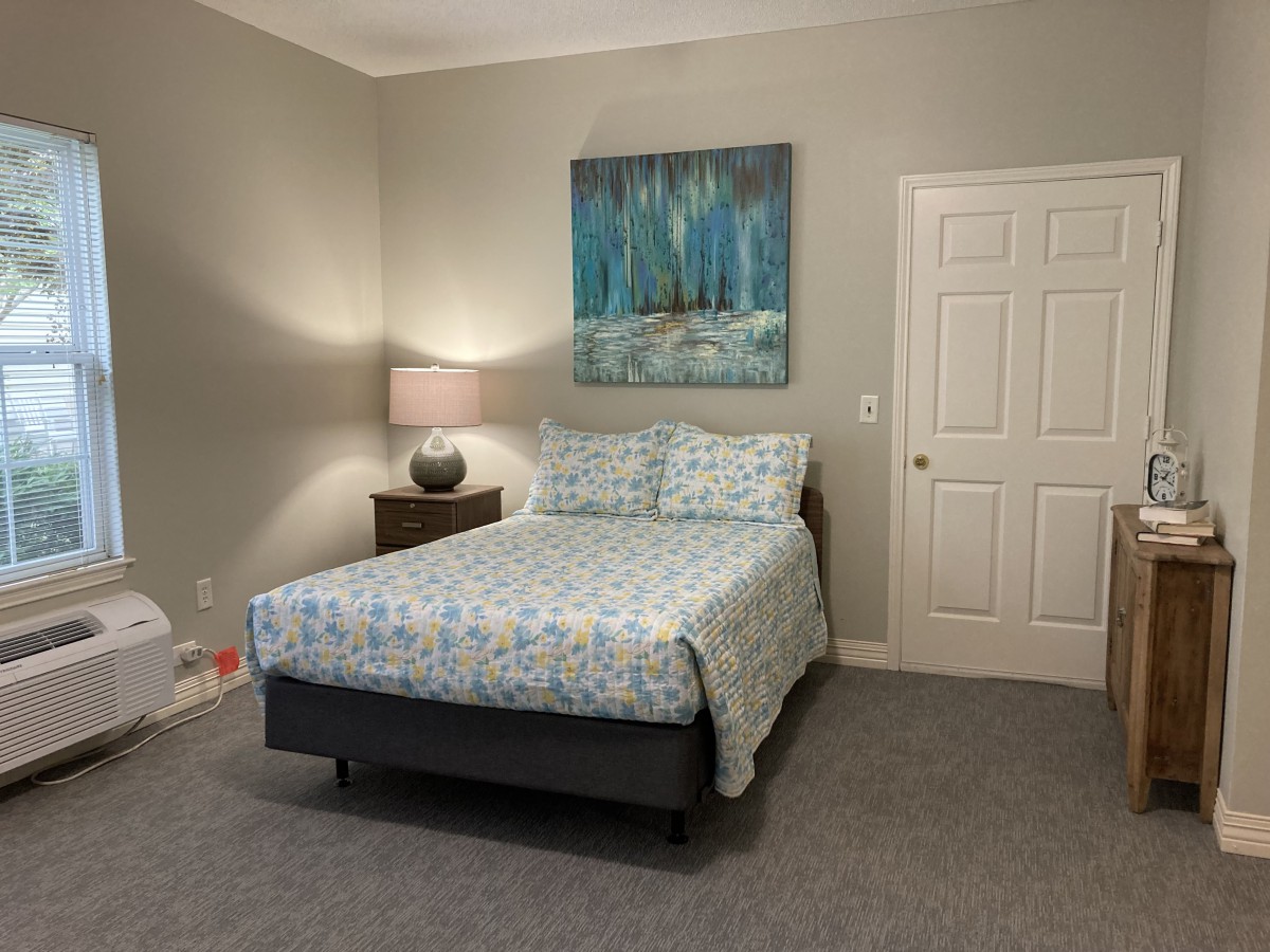 A cozy bedroom featuring a bed with patterned bedding, a nightstand with a lamp, and a large painting on the wall.